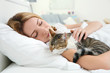 © Africa Studio - Cute cat and young woman relaxing on bed