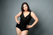 Beautiful overweight woman in black swimsuit on grey background