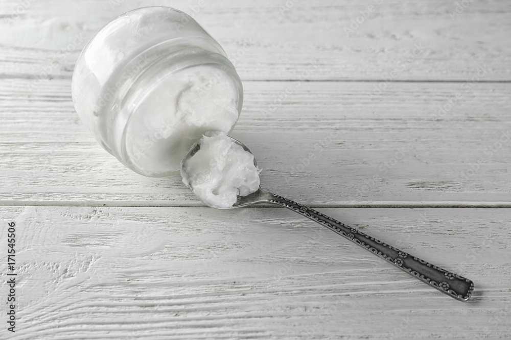 Spoon and jar with coconut oil on light wooden background
