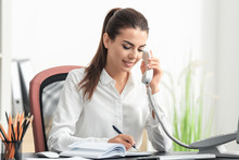 Young Female Receptionist Talking On Phone In Office