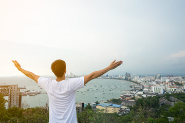 young man happy with hands rise up on beautiful bay and city Landscape with beautiful cloudy sky, sea.