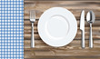 Blau karierte Tischdecke mit Teller, Messer und Gabel auf einem alten Holztisch