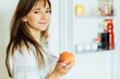 © Iryna - Healthy eating concept. Diet. Close up of charming brunette woman in pajamas holding peach in hands near the fridge with healthy food. Fruits and vegetables in the refrigerator. Vegan food