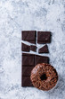 Chocolate glazed donut on chopped chocolate over gray texture background. Top view with space