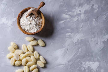 Wall Mural - Raw uncooked potato gnocchi with olive wood bowl of flour, grated parmesan cheese over gray concrete background. Top view with copy space. Home cooking.