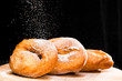 close-up of sweet fresh delicious donuts sprinkled with powdered sugar on round wooden board, dark background