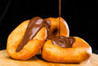 close-up of sweet fresh delicious donuts throwing with chocolate on round wooden board, dark background