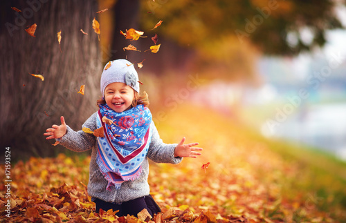 Plakat urocza dziewczynka szczęśliwy grając z opadłych liści w parku jesienią