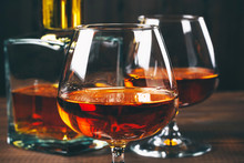 Two Glasses Of Brandy Or Cognac And Bottle On The Wooden Table.