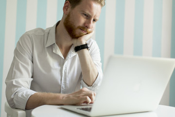 Wall Mural - Young redhair man working on laptop in room by the blue striped wall