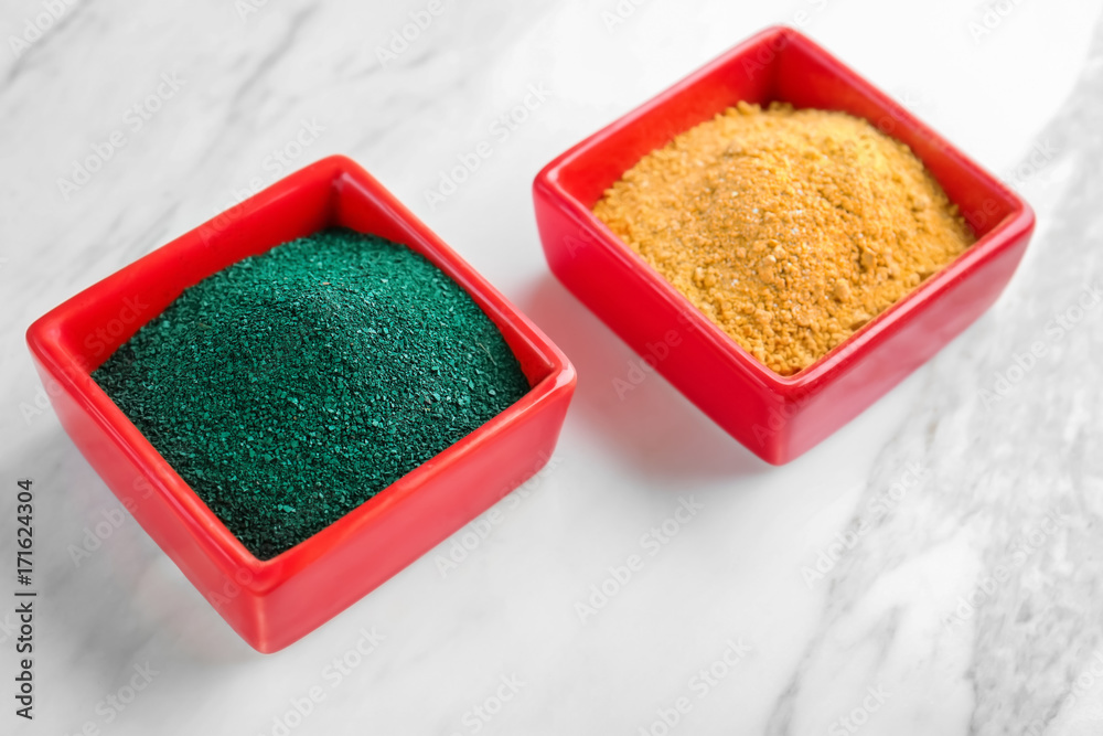 Spirulina and camu powders in red bowls on light background