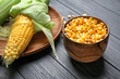 Fresh corn cob and bowl with kernels on wooden background
