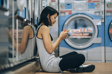 Young Asian Woman Waiting In A Laundromat