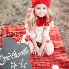 Wall Mural - Smiling baby girl 3-4 year old wearing red knitted hat and scarf outdoors. Looking at camera. Holiday season. Childhood.