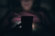 © Bogdan - Close-up. A young girl is typing on a smartphone. Lying in bed. Blurred dark background. At night