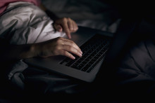 Close-up. A young girl has put her hands on the laptop keyboard. Lying in bed. Blurred dark background