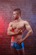 Young ripped man bodybuilder with perfect abs, shoulders,biceps, triceps and chest posing on brick wall background