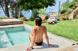 © Guille Faingold/Stocksy - Back view of wet-haired brunette sitting topless at pool