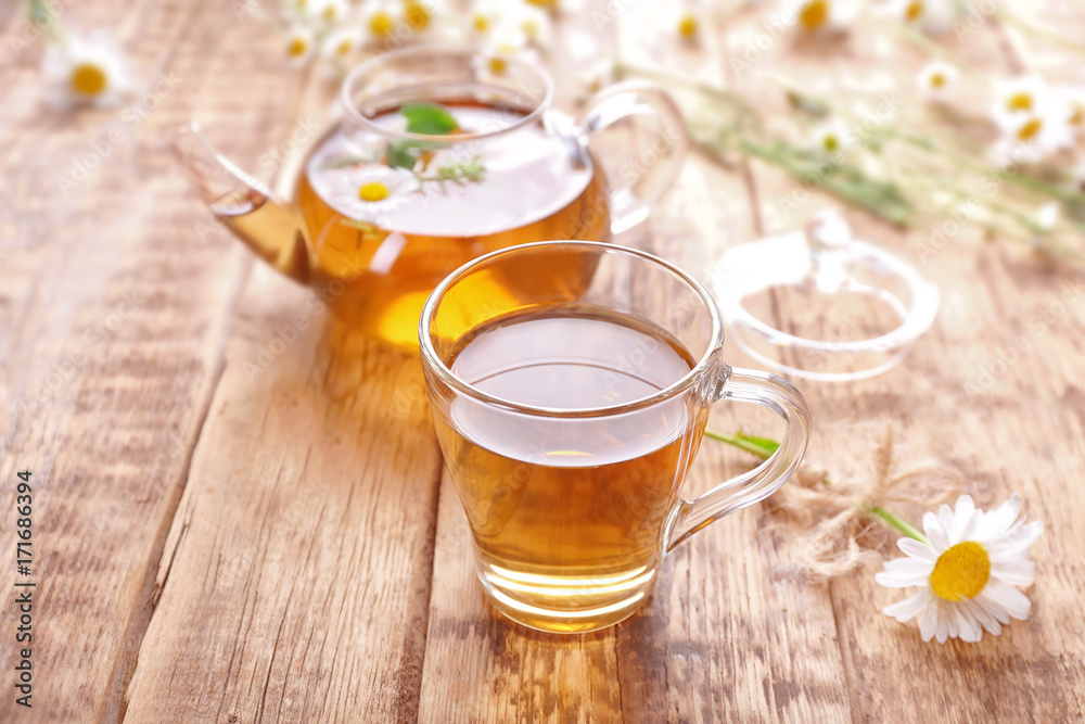 Cup of chamomile tea and teapot on wooden background