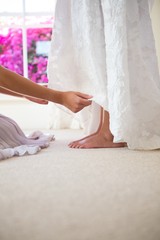 Wall Mural - Bridesmaid adjusting bride dress in fitting room