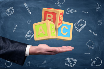Poster - A businessman's hand turned palm up with big ABC blocks hovering above it.