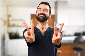 Handsome man with beard making victory gesture inside house