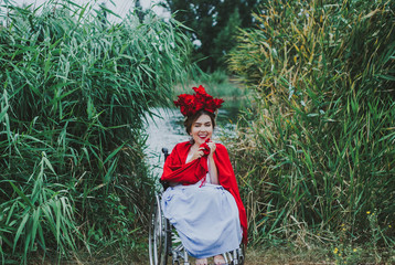 Summer conceptual portrait of beautiful young caucasian woman with red lips, red flowers in hair, sitting in wheel chair. frame with leaves wall on background.