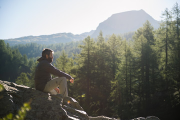 young adult active man sitting on top rock looking at panorama in sunny spring summer morning on mou