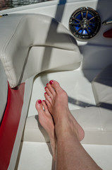 Woman's feet, crossed at the ankles, stretched out on the back seat of a leisure boat. Fun and relaxation enjoying the outdoor recreation activity of boating.