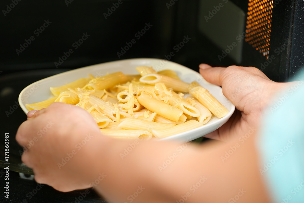 Woman putting plate with pasta into microwave oven. Cooking for one concept