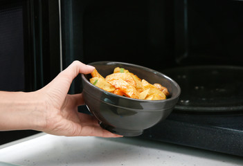 Sticker - Woman putting bowl with dinner into microwave oven. Cooking for one concept