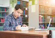 © kwanchaichaiudom - Young student taking notes from a book at library