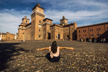 Girl sitting on a cobble-stone street to view Castello Estense of Renaissance town of Ferrara