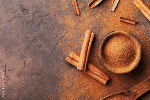 Fotografía Heap of cinnamon sticks and powder on brown rustic background top view