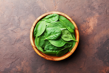 Wall Mural - Green baby spinach leaves in wooden bowl on rustic stone table top view. Organic healthy food.