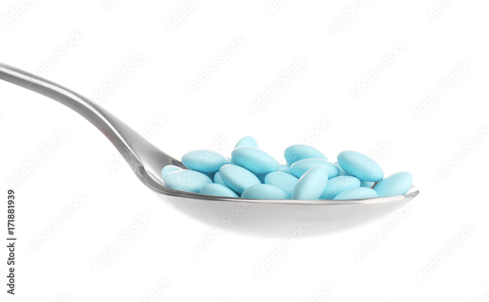 Spoon with colorful pills on white background