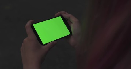 Wall Mural - handheld shot of female teen girl holding smartphone with green screen sitting outdoors