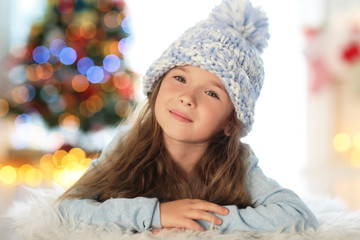 Happy little girl in hat lying on carpet at home