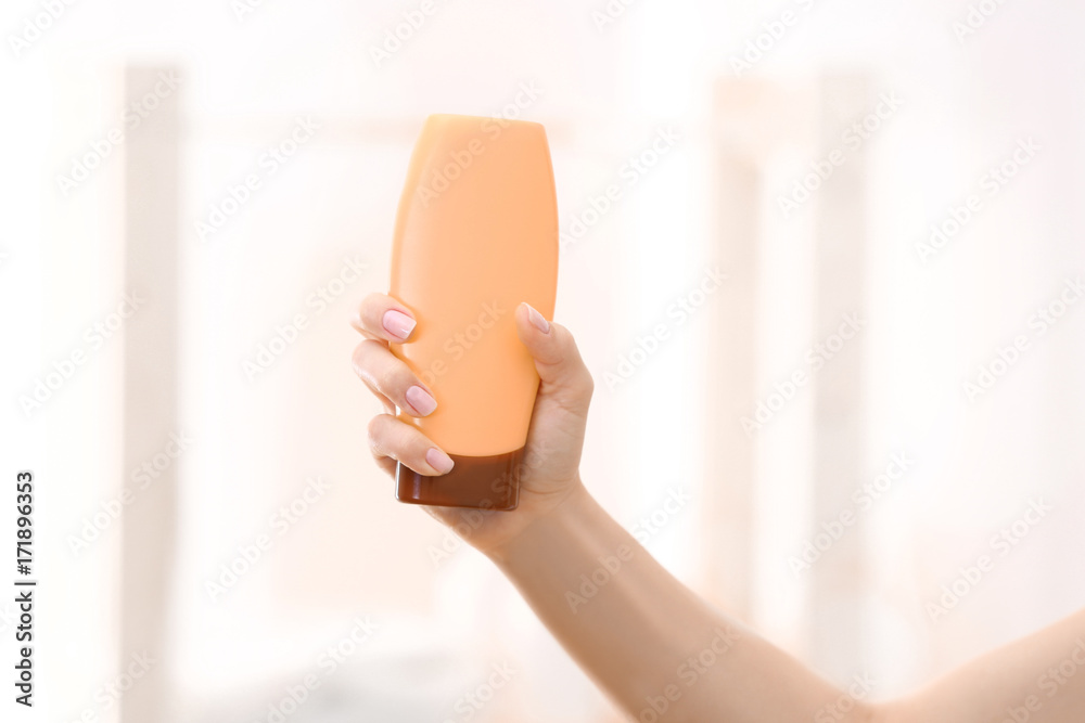Young woman holding bottle with cream on light background