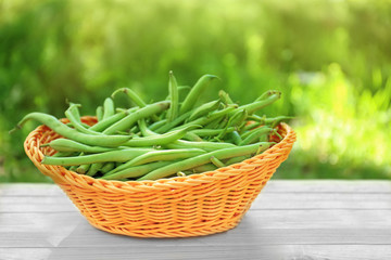 Wicker basket with raw fresh organic green beans on table outdoors