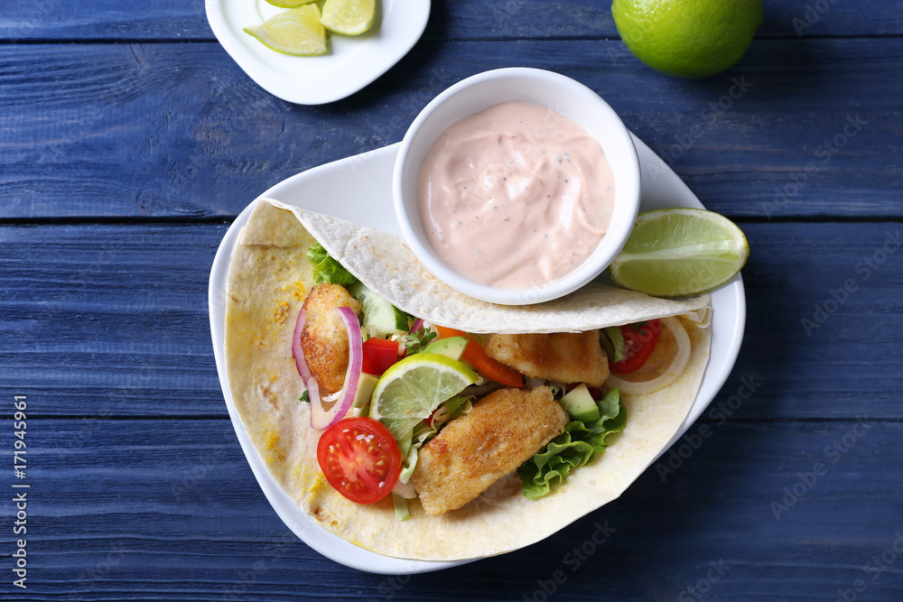Plate with tasty fish taco and sauce on wooden table