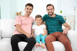 Male gay couple with foster son sitting on sofa at home. Adoption concept