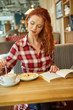 © ZoomTeam - Smiling red hair woman reading book at coffee shop