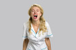 Young nurse screaming desperate on grey background. Close up shot of stressed and frustrated young doctor woman screaming with desperate and horrified expression.
