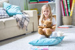 Portrait of adorable little girl with plush teddy bear in hands posing for photography while sitting on carpet at cozy living room