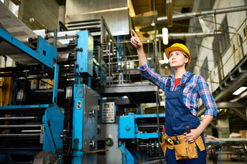 Portrait of talented factory worker in overall and checked shirt pointing at something while working at production department