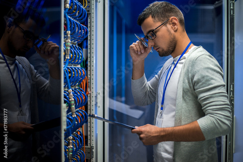Plakat Widok z boku portret młodego człowieka stojącego przez serwer szafy podczas pracy z superkomputera w centrum danych i przytrzymanie schowka