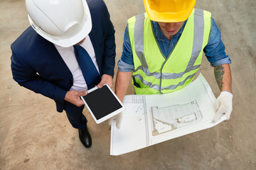 High angle view of unrecognizable foreman and architect studying blueprint while having working meeting at construction site