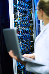 Unrecognizable female scientist working with supercomputer, focus on server cabinet with wires in background