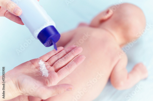 Fototapeta Mom applying talc powder from plastic tube to the baby body